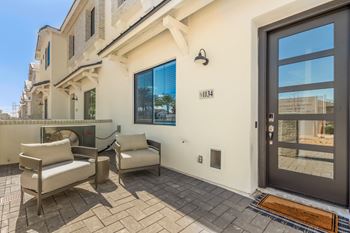 A modern house with a glass door and a patio with two chairs and a table.